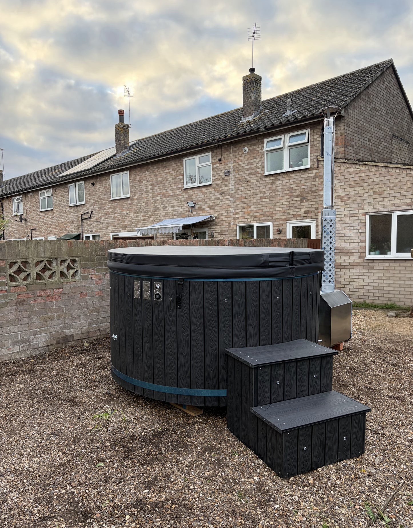 Black hot tub with steps in front of a residential house